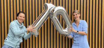 2 Frauen die Luftballons in der Form einer 1 und einer 0 in die Luft halten, um das 10 jährige Jubiläum zu feiern