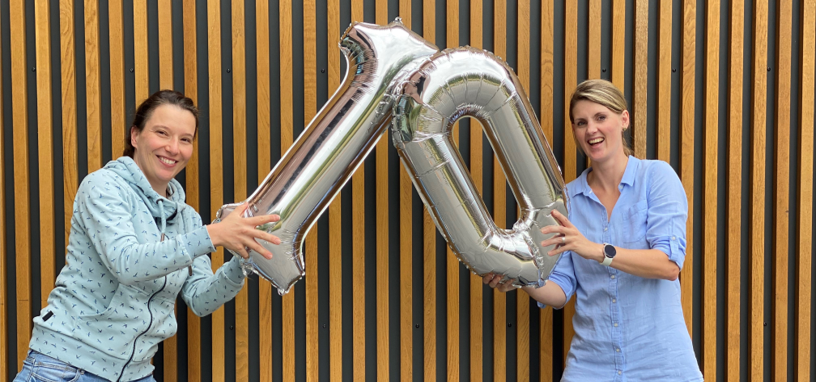 2 Frauen die Luftballons in der Form einer 1 und einer 0 in die Luft halten, um das 10 jährige Jubiläum zu feiern